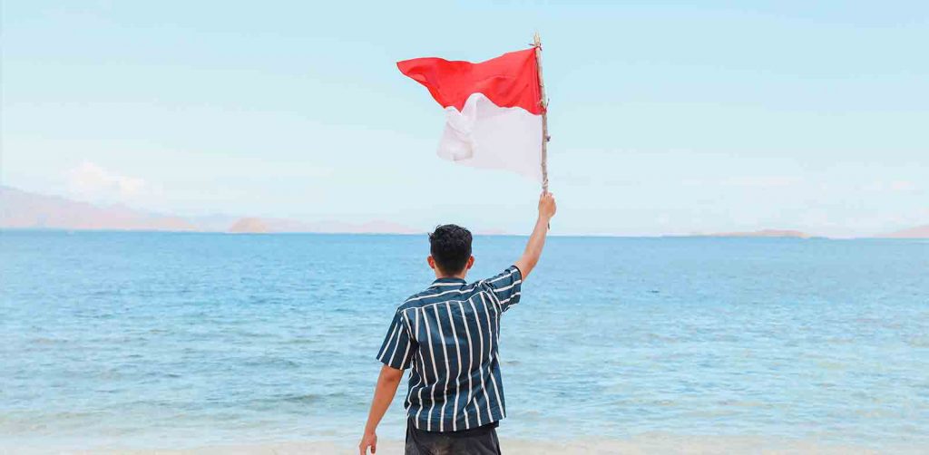 seorang  travel influencer indonesia sedang mengibarkan bendera merah putih di pantai