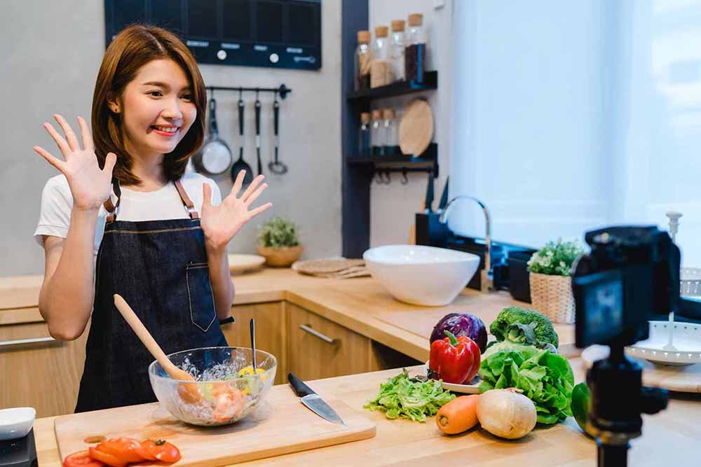 seorang wanita vlogger makanan sedang membuat konten di dapurnya dengan kamera