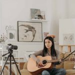 seorang content creator wanita sedang merekam dirinya dengan gitar